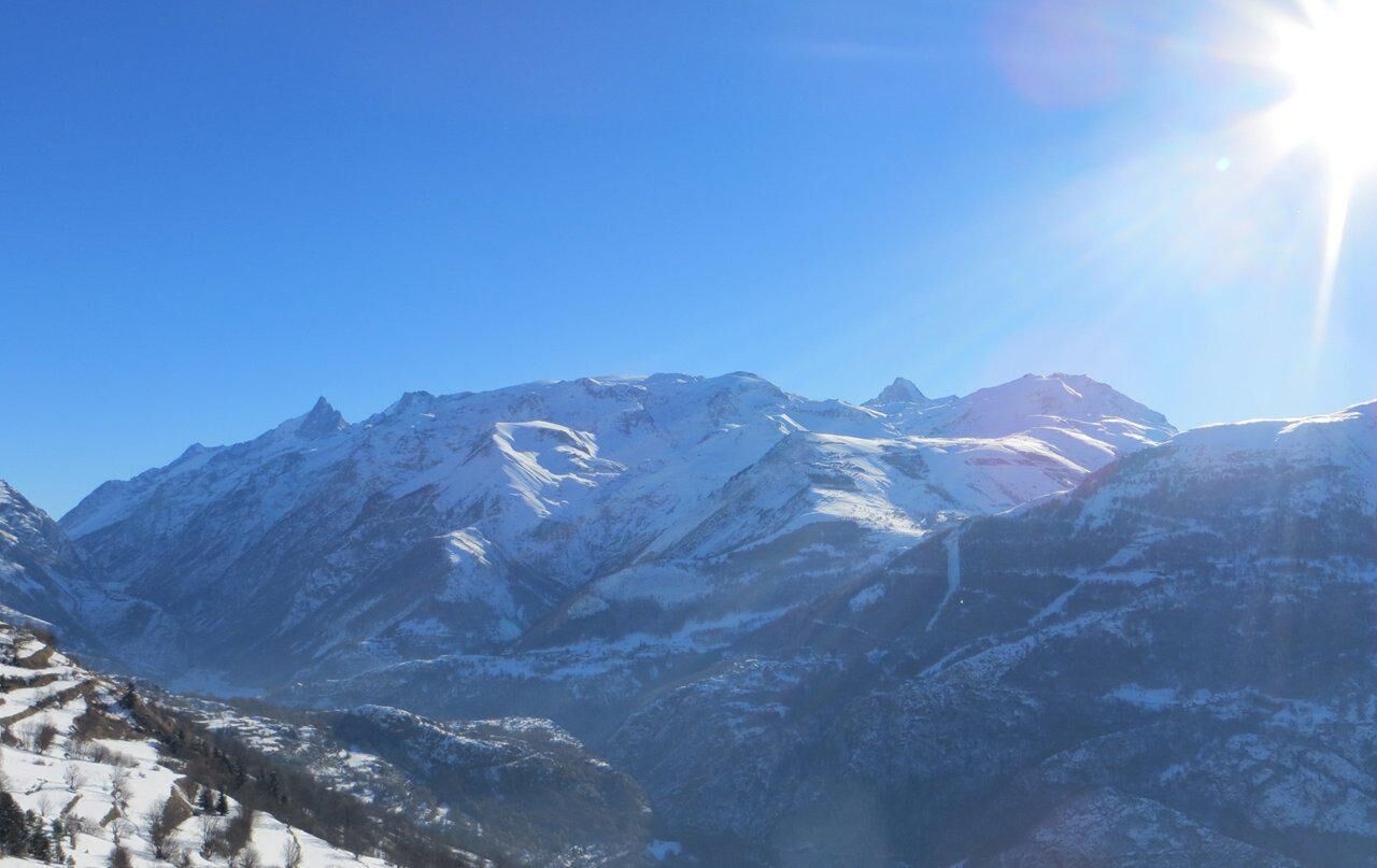 Une chaîne de montagnes enneigée, sous un ciel dégagé et baignée de soleil.