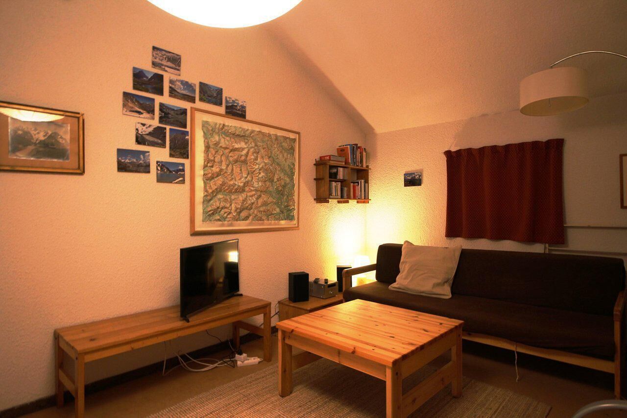 Ein gemütliches Wohnzimmer mit einem Holztisch, einem Fernseher auf einem Schrank, einem Bücherregal, einer großen gerahmten Karte und einem roten Vorhang.
