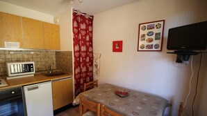 A compact kitchen with wooden cabinets, a microwave, a sink, and a small table with chairs. - 300m from ski slopes, view mountain/swimming pool, balcony, tv, ski locker, 17m², Auris en Oisans (Auris)