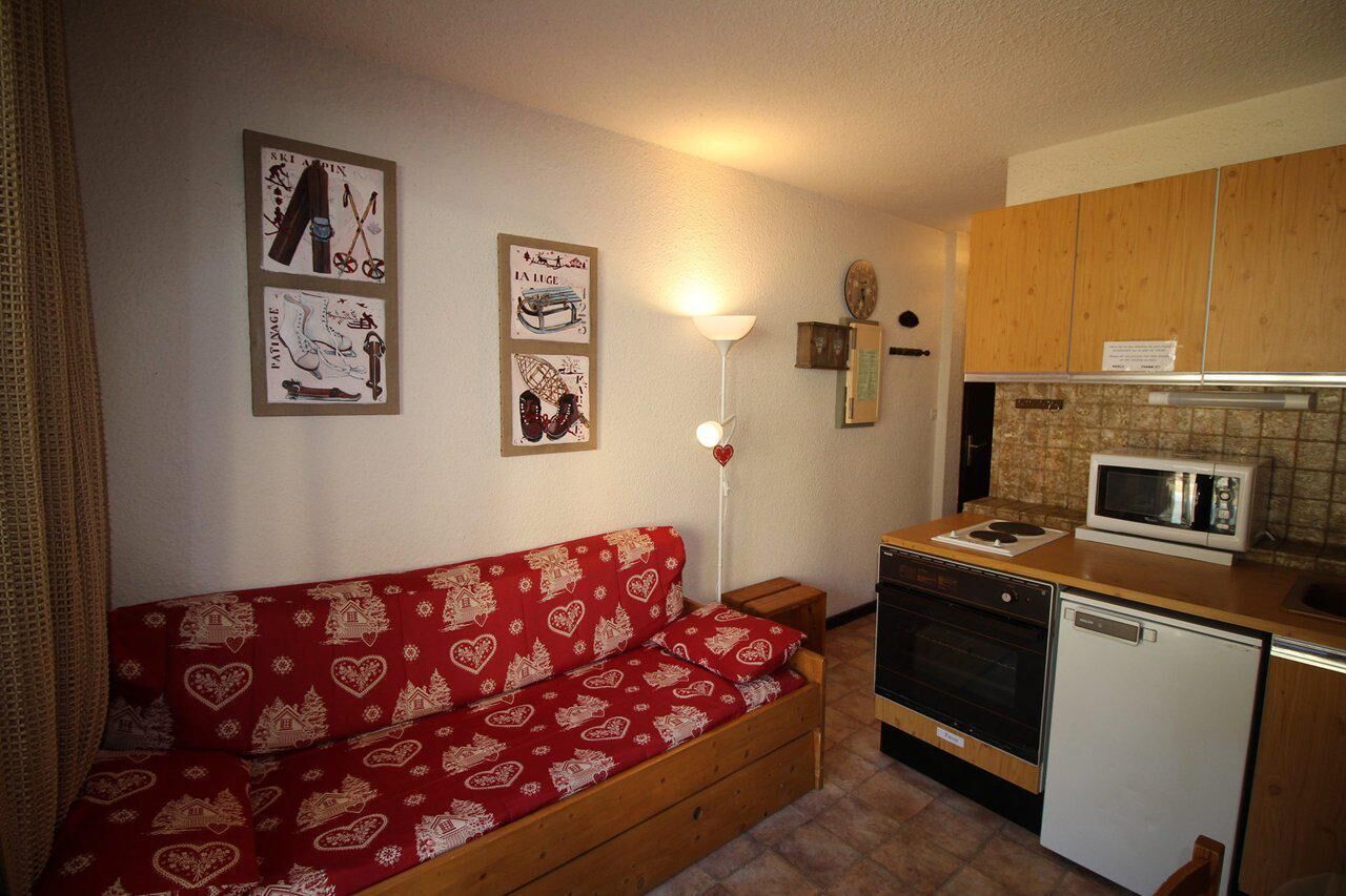 A compact kitchen with wooden cabinets, a microwave, an oven, and a dishwasher. A red sofa with heart patterns is against the wall.