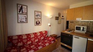 A compact kitchen with wooden cabinets, a microwave, an oven, and a dishwasher. A red sofa with heart patterns is against the wall. - 300m from ski slopes, view mountain/swimming pool, balcony, tv, ski locker, 17m², Auris en Oisans (Auris)