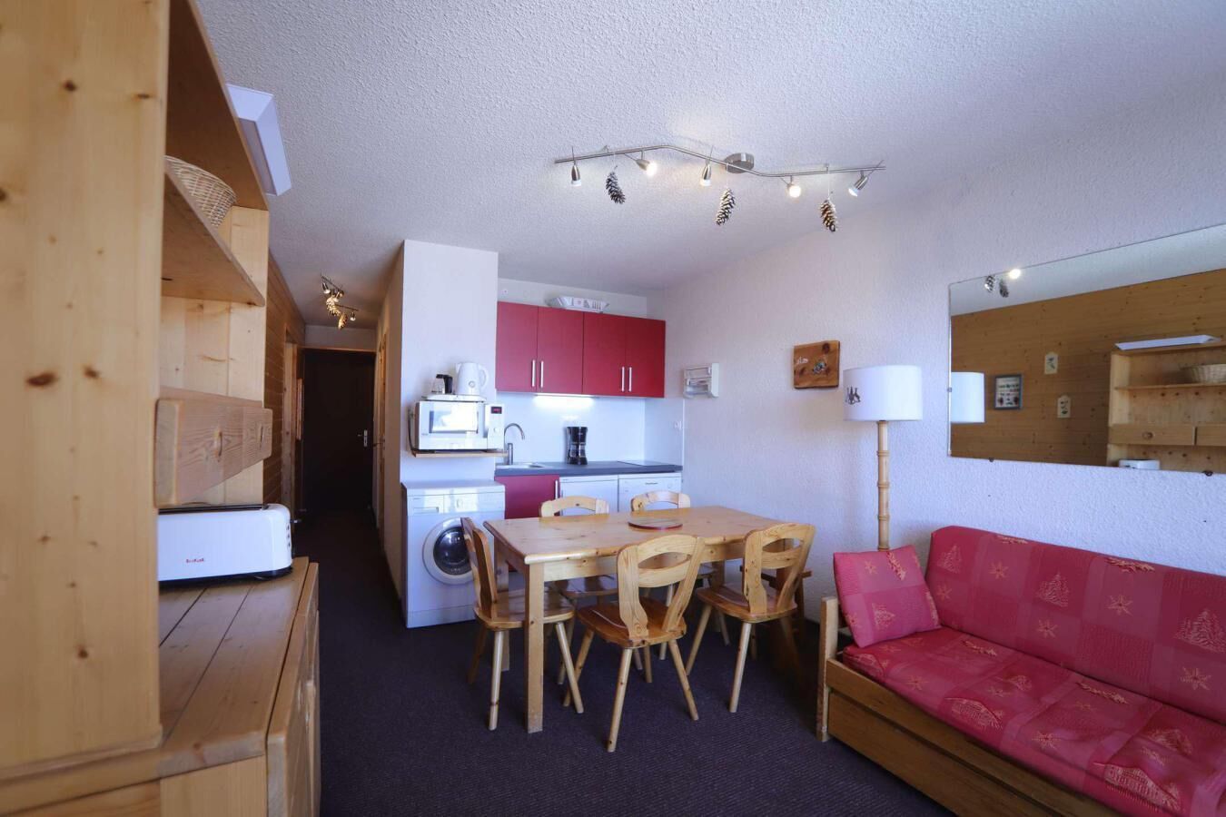 A compact living space with a kitchenette, dining area, and a red sofa.
