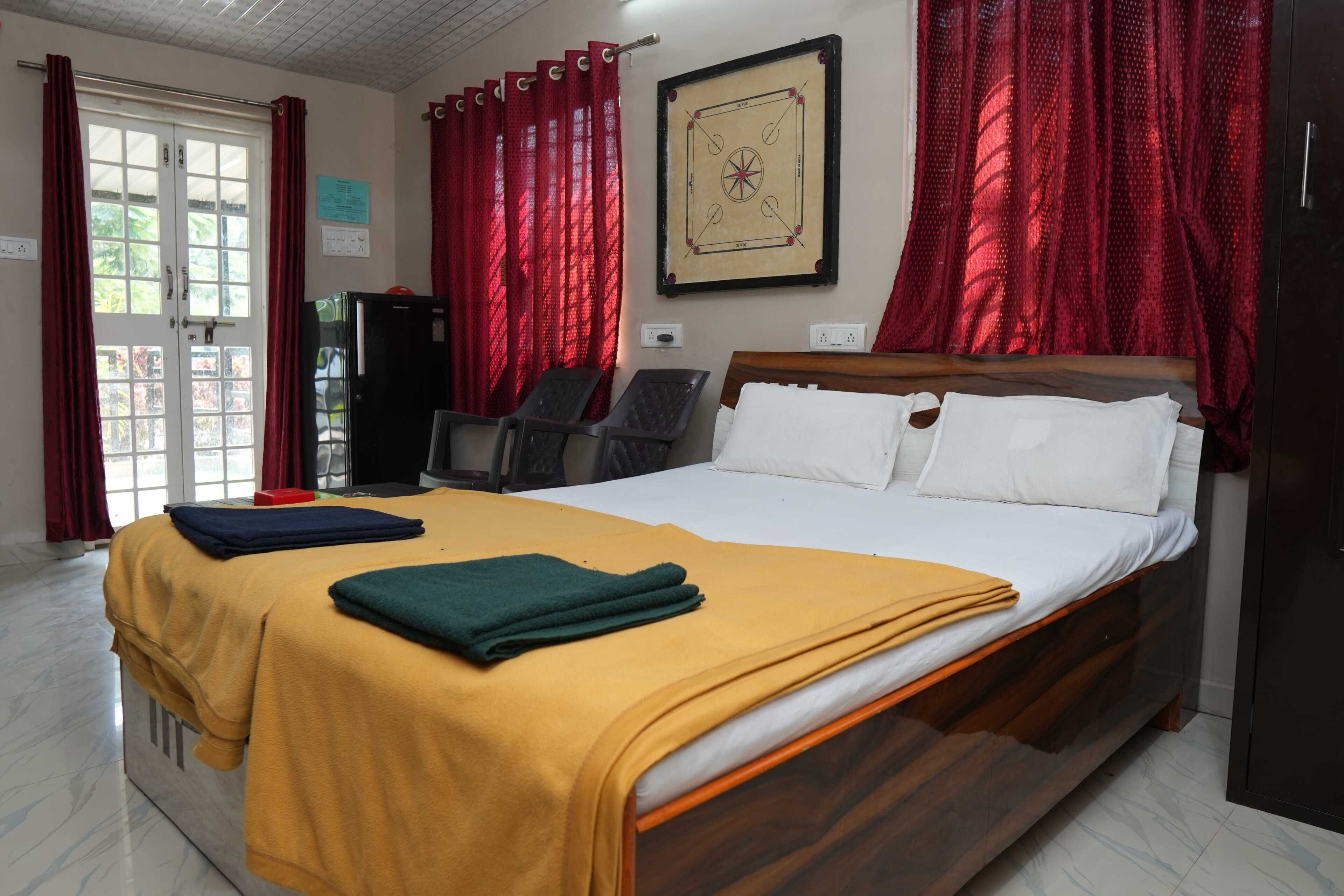 A hotel room with a bed, a desk, a chair, a wardrobe, and a window with red curtains.