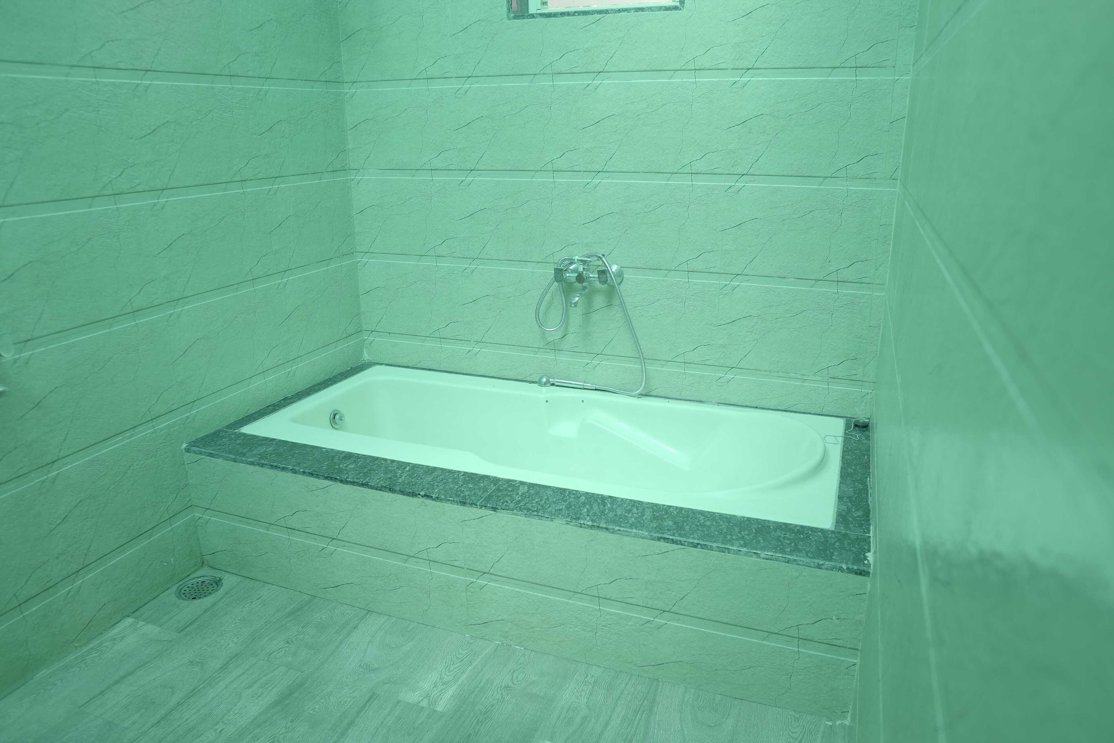 Un baño con una bañera rectangular, paredes de azulejos y un desagüe.