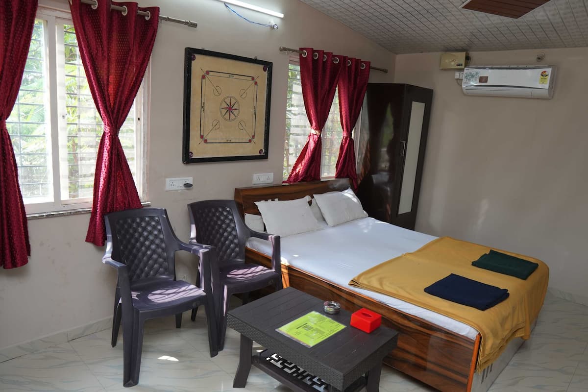 A hotel room with a bed, two chairs, a small table, and a framed picture on the wall.
