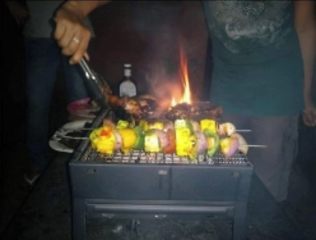 A person grilling skewers with various vegetables on a portable grill.