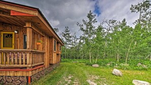 Une cabane en bois dotée d’un porche, entourée d’une zone boisée et accessible par un sentier de terre.