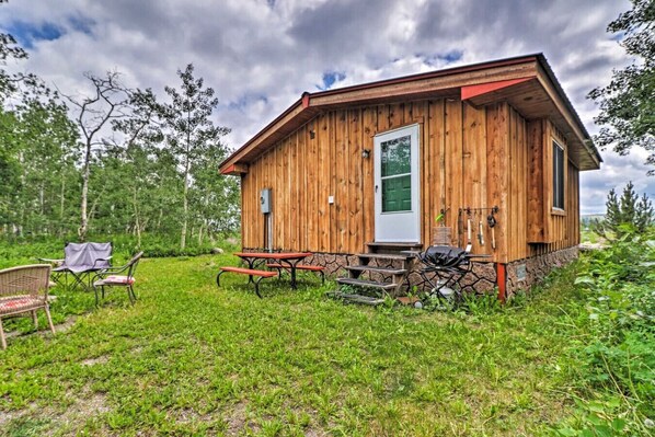 Eine Holzhütte mit Eingangstür, einer kleinen Veranda und einem Picknicktisch mit Bänken.