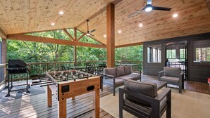 An outdoor deck with wooden flooring, a foosball table, seating area, and a barbecue grill. - Sage Creek: Secluded Family Getaway | Large Deck (Broken Bow)