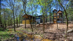 A cabin with a wooden exterior, surrounded by trees and a small stream. - Sage Creek: Secluded Family Getaway | Large Deck (Broken Bow)