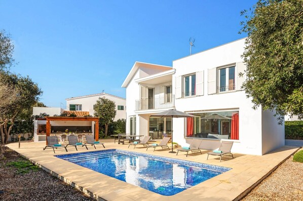 A modern two-story house with a swimming pool, outdoor seating, and a covered patio area.