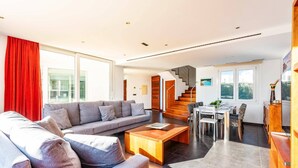 A modern living room with a grey sofa, wooden coffee table, and a dining area with a wooden table and chairs.