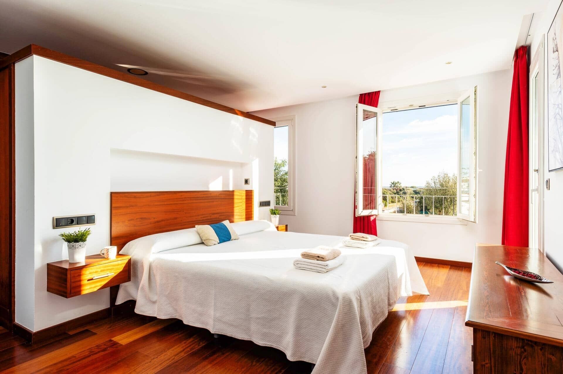 A bedroom with a large bed, bedside tables, a nightstand, a window with a view, and a wooden floor.