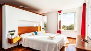 A bedroom with a large bed, bedside tables, a nightstand, a window with a view, and a wooden floor.
