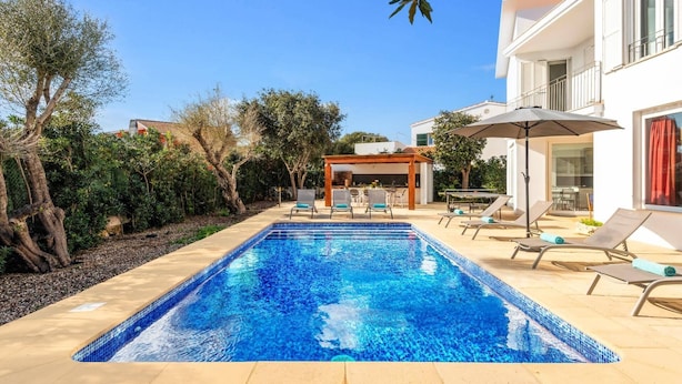 A modern pool area with a clear blue pool, lounge chairs, and a pergola.