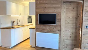 A modern kitchen with white cabinets, a built-in oven, and a flat-screen TV mounted on a wooden wall. - 20m from ski slopes, 3rd floor, balcony, parking, 50m², Vars (Vars)
