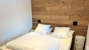 A neatly made bed with white bedding and pillows, a wooden headboard, and a bedside table with drawers. - 20m from ski slopes, 3rd floor, balcony, parking, 50m², Vars (Vars)