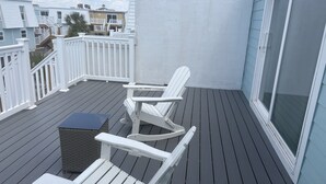 Un balcón con dos sillas Adirondack blancas, una mesita de mimbre y vistas a casas vecinas.