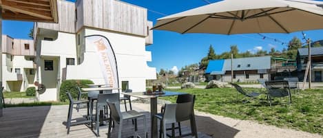 An outdoor dining area with tables and chairs, a wooden deck, and a building with a sign.