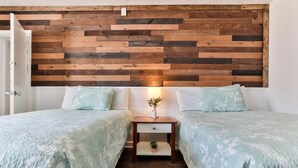 A bedroom with two beds, a wooden headboard, a bedside table with a lamp, and a small plant. - Pool View Studio Suite #109 (New Smyrna Beach)