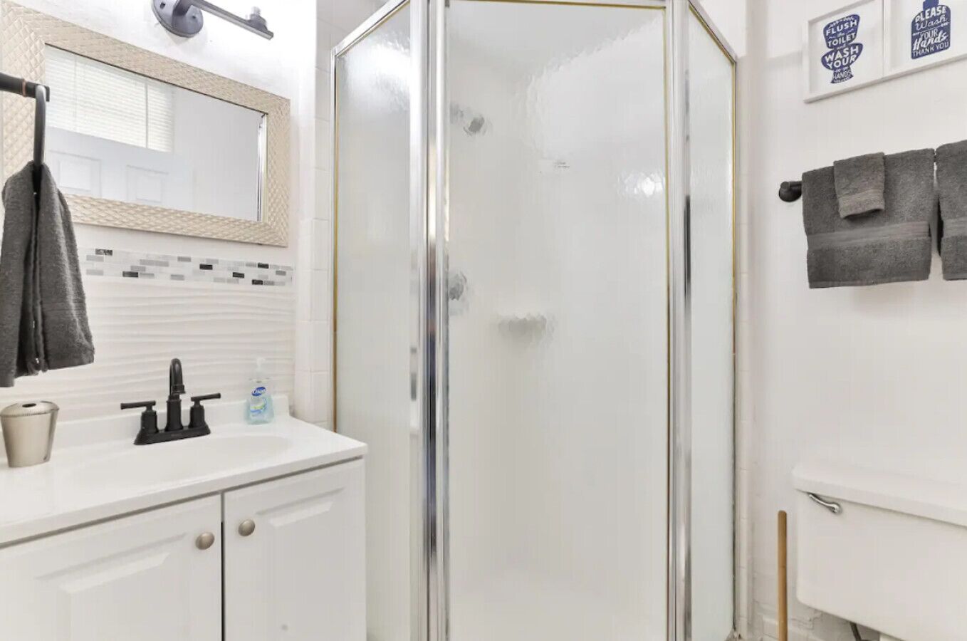 Een badkamer met een douche met glazen wanden, een wit wastafelmeubel met zeepdispenser en een spiegel erboven.