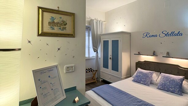 Ein Hotelzimmer mit einem Bett, einem Schreibtisch mit Lampe, einem gerahmten Bild, einem Wandzeichen und einem Kleiderschrank.