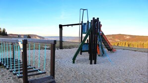 A playground with climbing structures and a slide, set against a backdrop of hills and a clear sky.