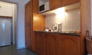 Een keuken met houten kastjes, een magnetron, een koffiezetapparaat en een spoelbak.