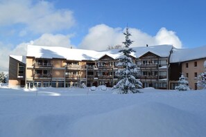 Een meerlaags hotel met een met sneeuw bedekte buitenkant, balkons en een heldere lucht.