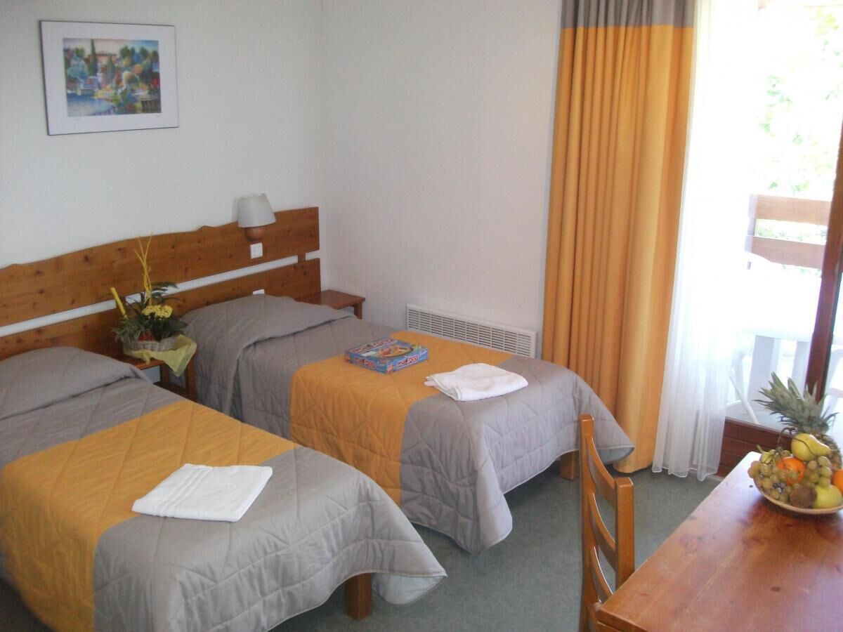 Een hotelkamer met twee bedden, een houten hoofdeinde, een tafel met een schaal fruit en een raam met gordijnen.