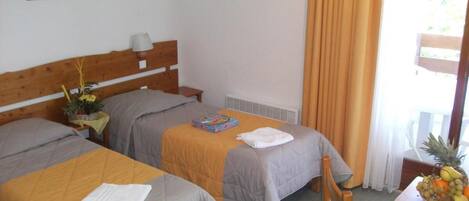 Een hotelkamer met twee bedden, een houten hoofdeinde, een tafel met een schaal fruit en een raam met gordijnen.