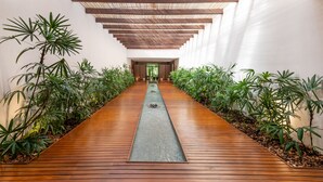 A corridor with wooden flooring, green plants on either side, and a central water feature. - Luxury 4-Bedroom Condo with Stunning Views – Poro 4A (Santa Cruz)