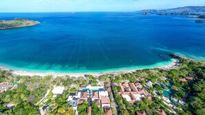 An aerial view of a coastal resort with a large pool, beachfront, and lush greenery. - Luxury 4-Bedroom Condo with Stunning Views – Poro 4A (Santa Cruz)