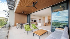 A modern balcony with a wooden ceiling, a dining area with green chairs, a sofa, and a view of the interior. - Luxury 4-Bedroom Condo with Stunning Views – Poro 4A (Santa Cruz)