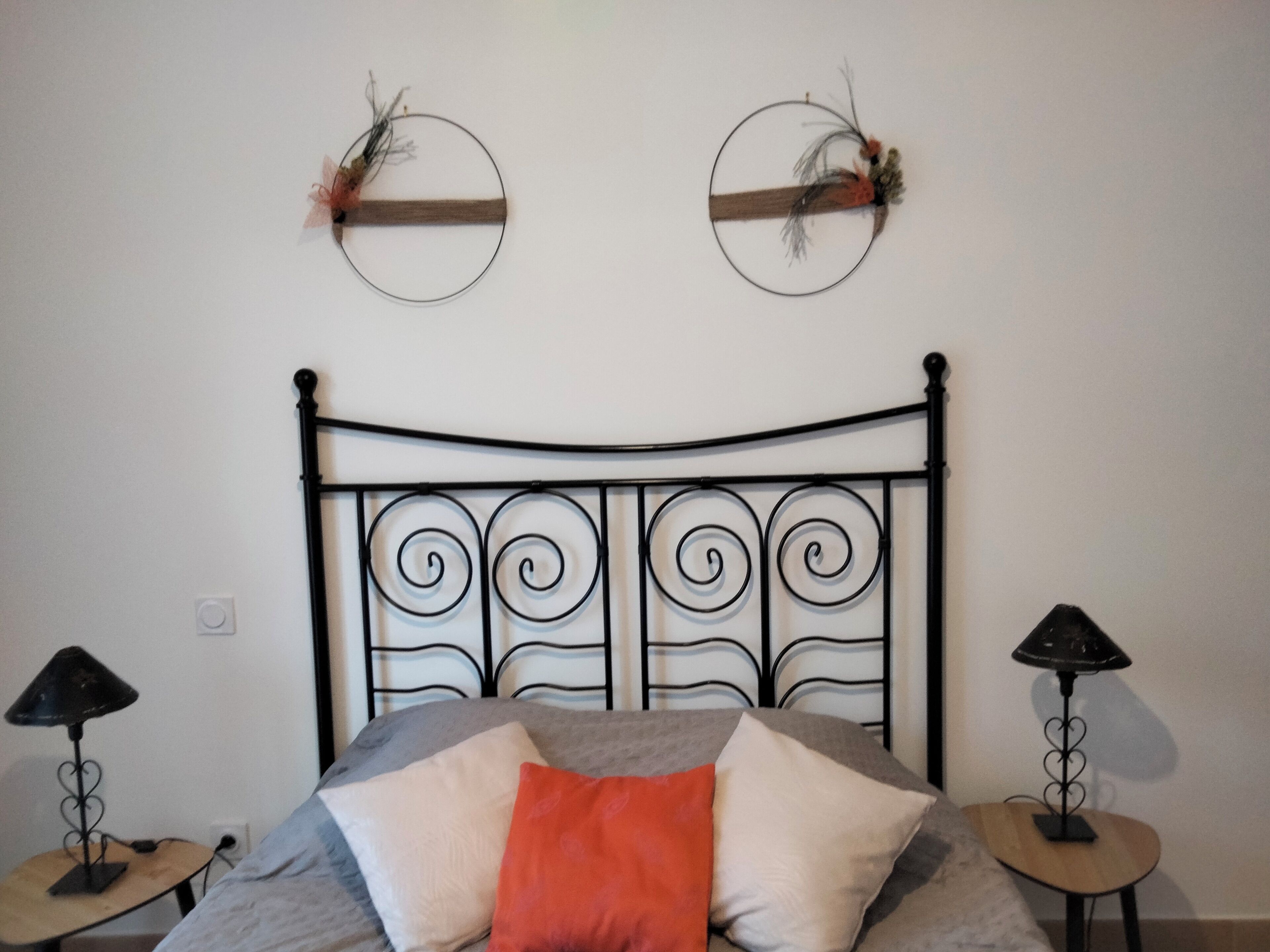 Una cama con cabecera de metal, dos adornos en la pared y dos mesitas de noche con lámparas.