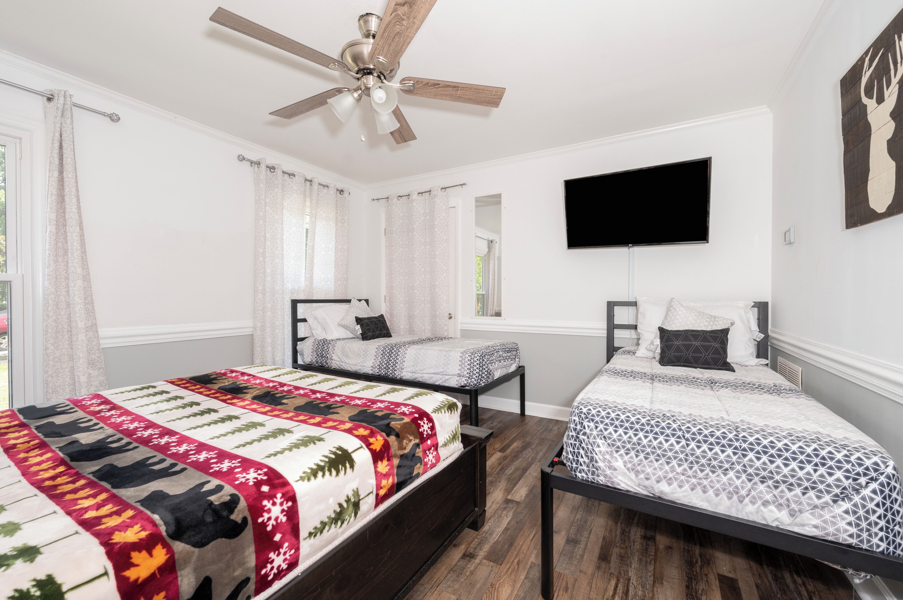 A bedroom with two beds, a ceiling fan, a mounted TV, and a deer head artwork.