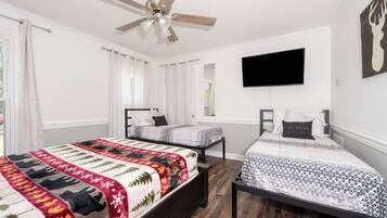 A bedroom with two beds, a ceiling fan, a mounted TV, and a deer head artwork.