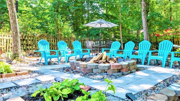 A patio with blue Adirondack chairs, a fire pit, and an umbrella. - King beds Hot Tub Arcade Luxury Showers (Kernersville)