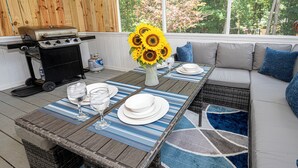 A covered patio with a dining table set for four, a grill, and a sofa with cushions. - King beds Hot Tub Arcade Luxury Showers (Kernersville)