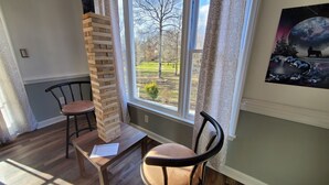 A room with a wooden table, two chairs, a brick wall, and a window with a view of a park. - King beds Hot Tub Arcade Luxury Showers (Kernersville)