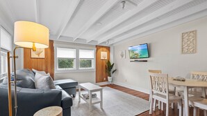 Una sala moderna con sofá, mesa de centro, mesa de comedor y sillas. Hay un televisor en la pared y una planta en maceta en el suelo.