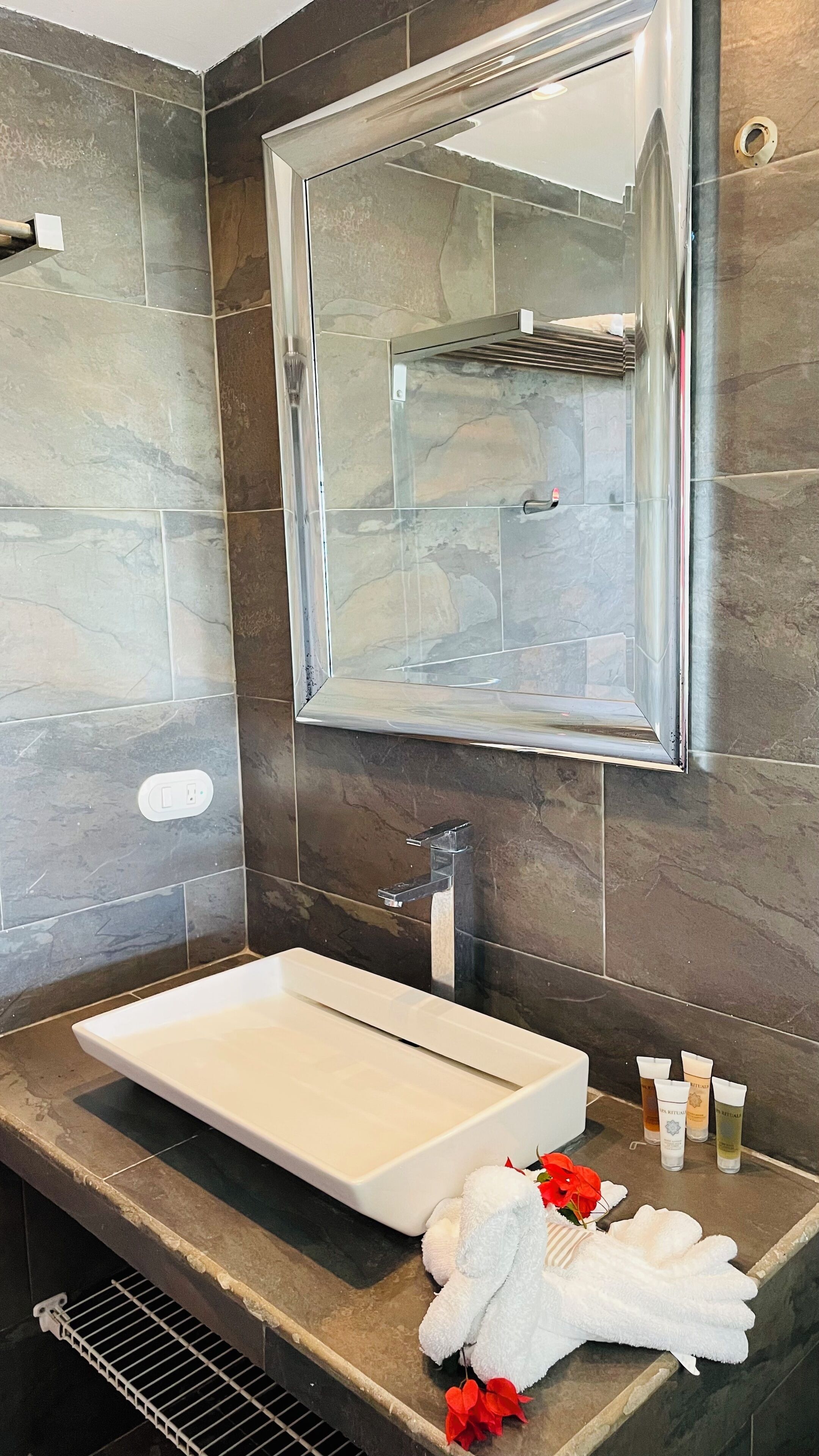 A modern bathroom with a large mirror, a rectangular sink, and toiletries on the counter.