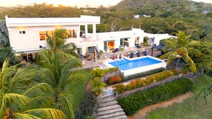 Une villa moderne dotée d’une piscine, entourée d’une végétation luxuriante et de palmiers.