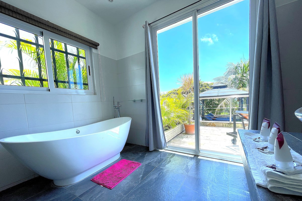 Ein modernes Badezimmer mit freistehender Badewanne, einer Duschkabine aus Glas und Blick ins Freie.