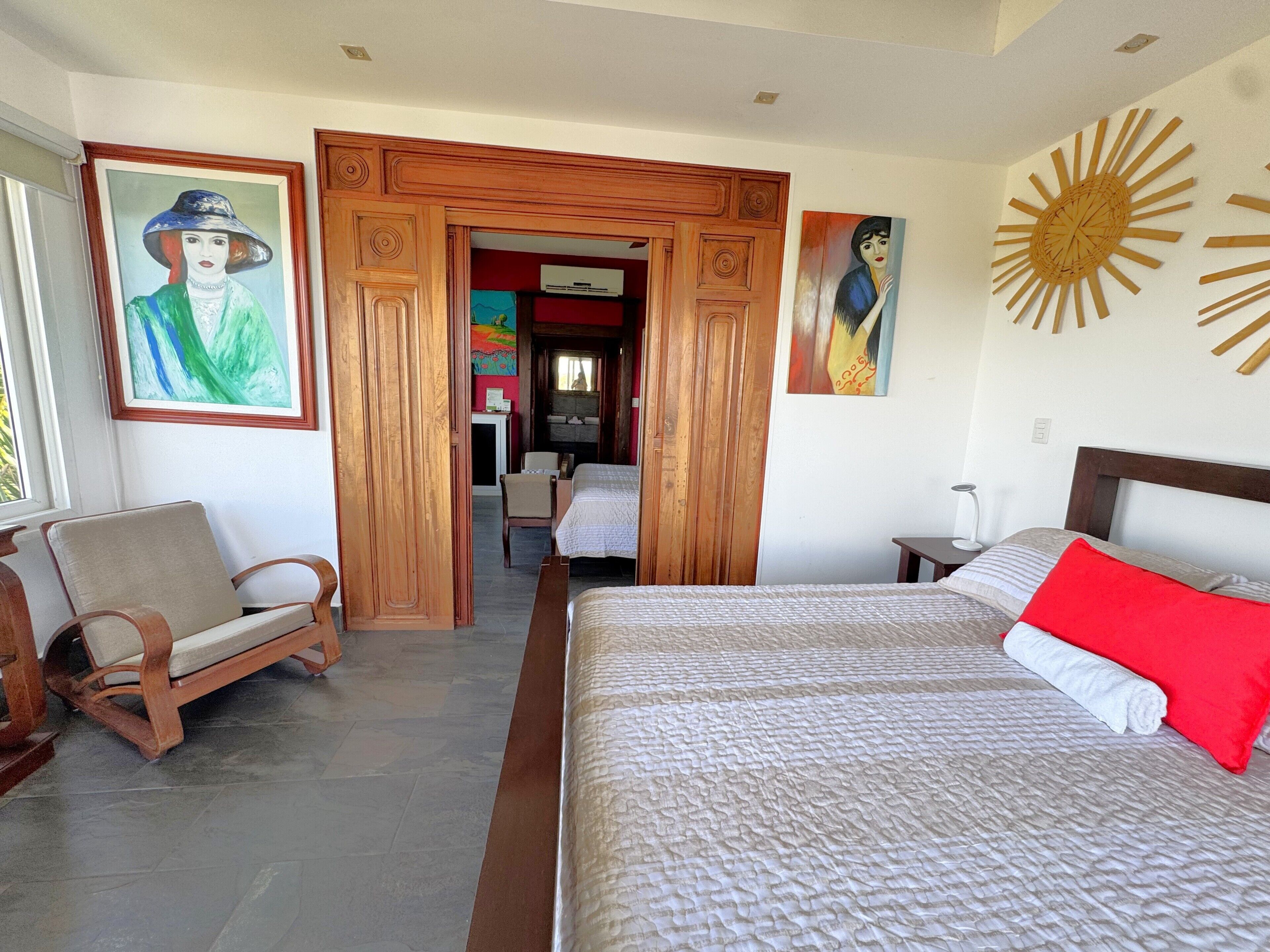 Una habitación de hotel con una cama, una silla, un escritorio y una puerta que da a otra habitación.