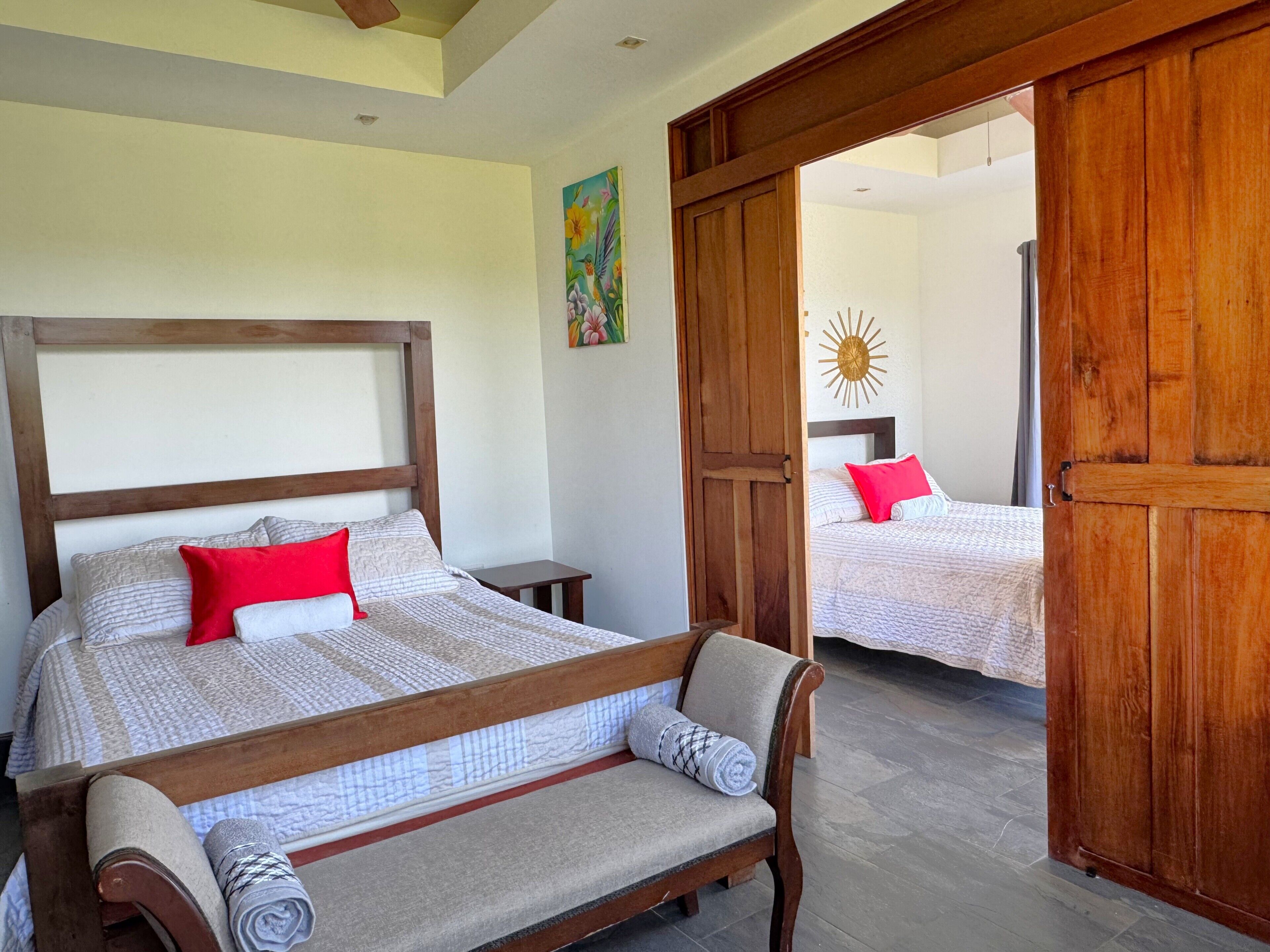 Un dormitorio con estructura de cama de madera, un banco y una puerta que da a otra habitación.