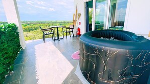 Un balcon doté d’un jacuzzi, d’une table et de chaises, offrant une vue sur un paysage luxuriant.