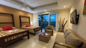 Une chambre d’hôtel avec deux lits, un canapé, une petite table et un balcon donnant sur des palmiers.