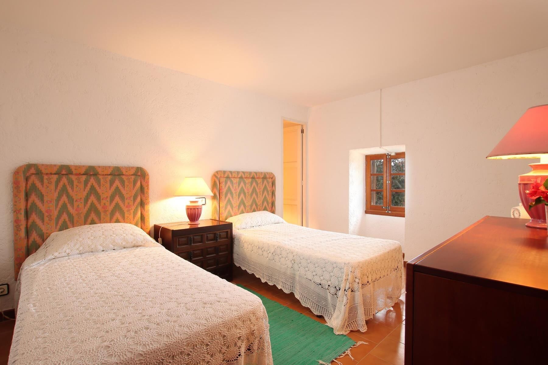 Een kamer met twee bedden, elk met een gestreept hoofdeinde, een nachtkastje met een lamp, een houten dressoir en een raam met uitzicht.