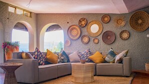 A modern living room with a grey sofa, patterned cushions, a woven coffee table, and a wall decorated with various woven plates. - Lake Alexander Country Resort  (Penhalonga)